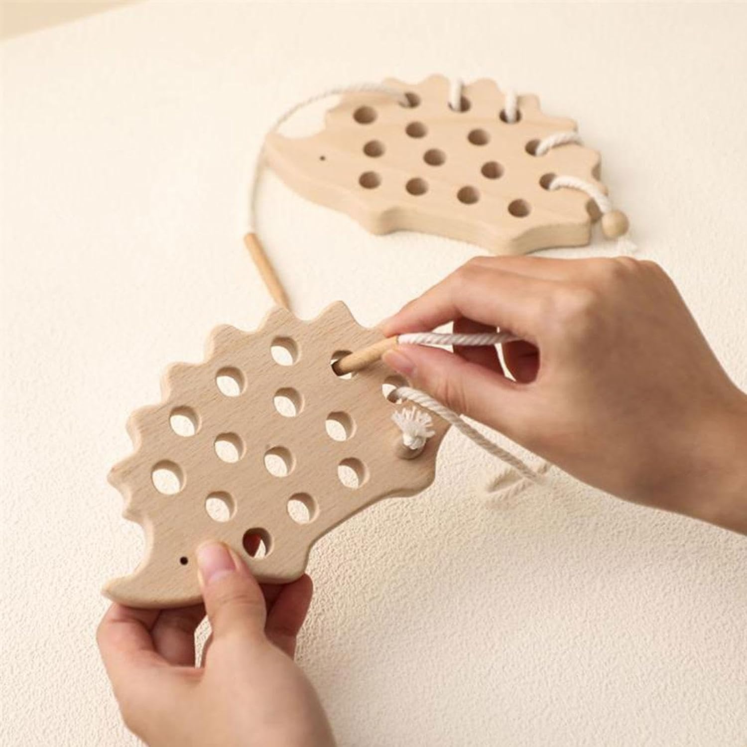 Child lacing the cotton cord through the wooden hedgehog threading toy