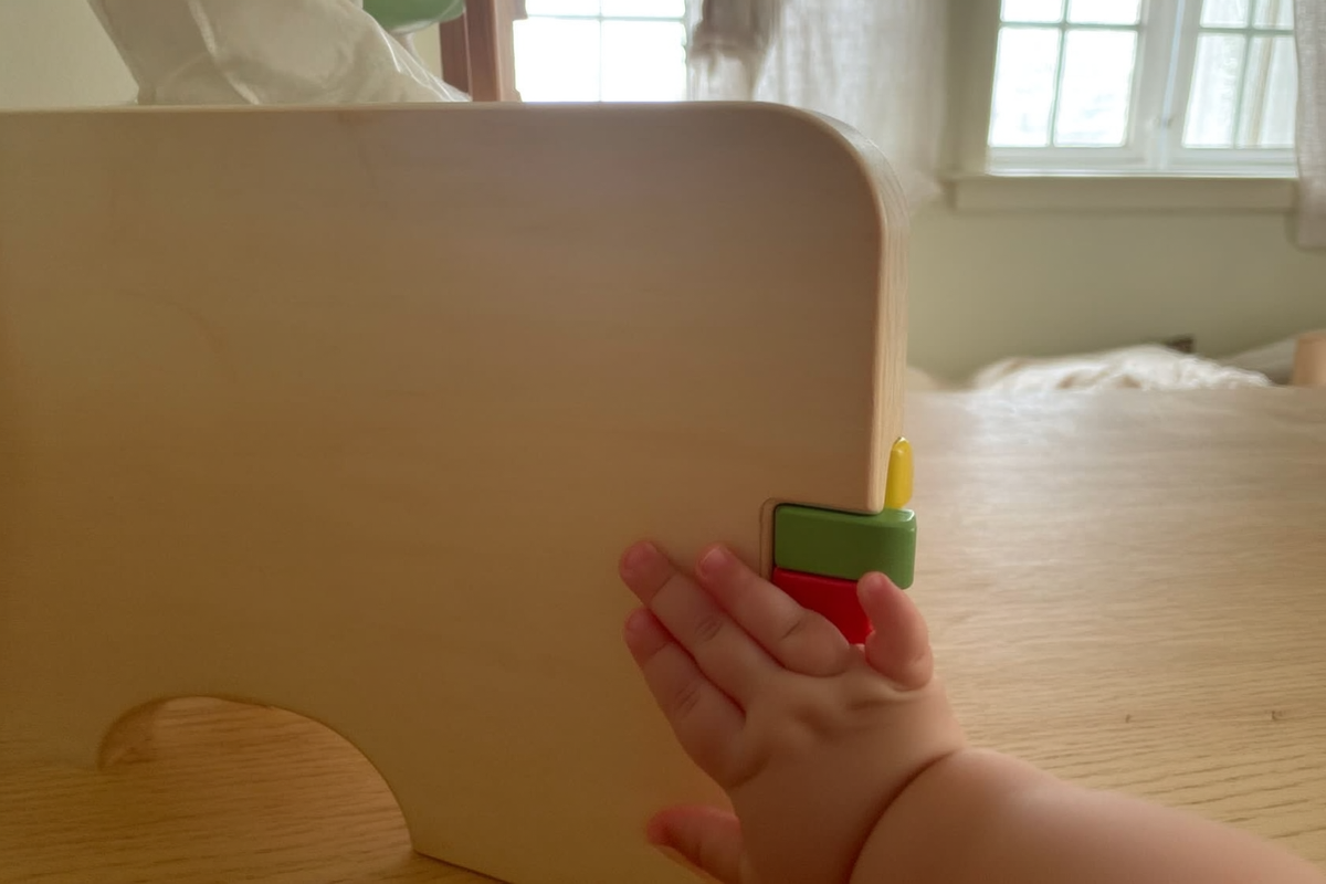A toddler's hand running along the smooth edge of a plain wooden toy