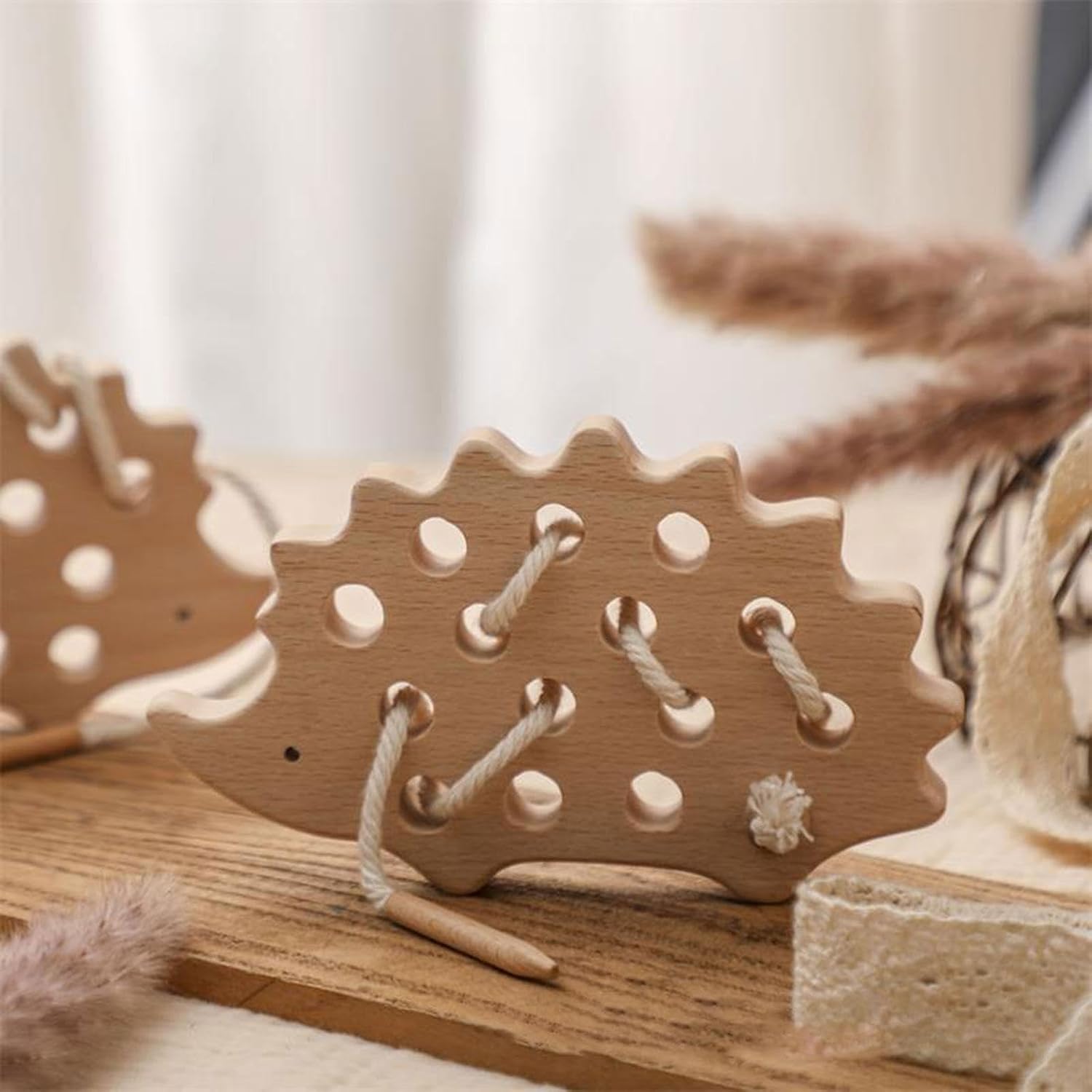 Wooden hedgehog lacing toy styled on a wooden board with dried grasses