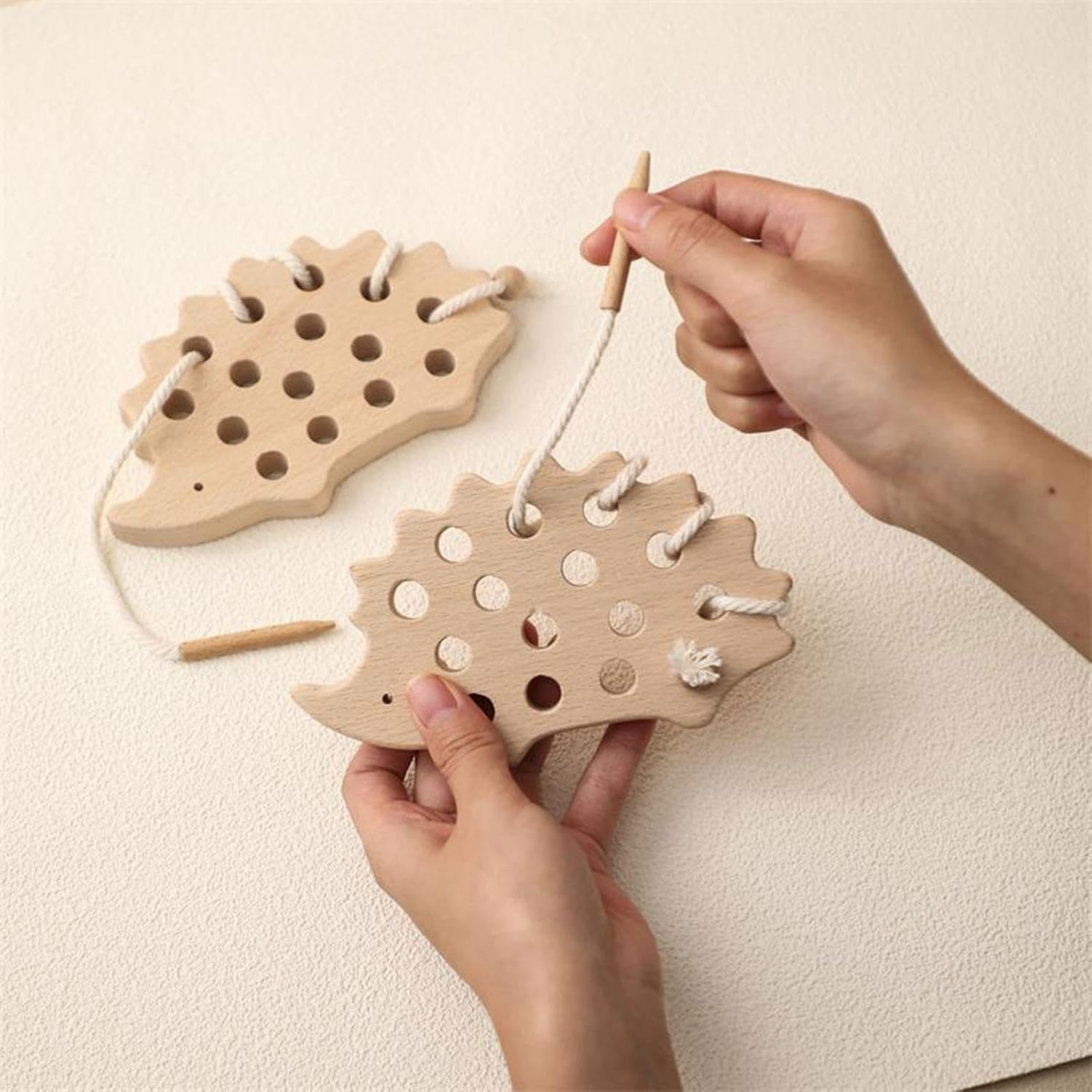 Hands threading the wooden needle through the hedgehog lacing toy
