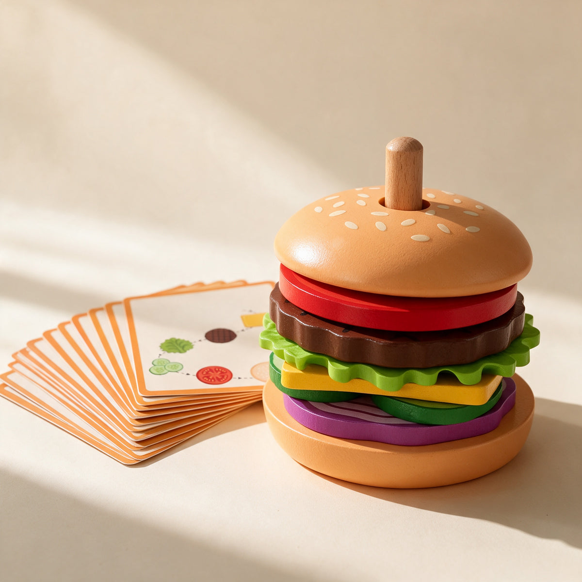 Wooden burger stacking toy fully assembled on its peg beside the recipe cards